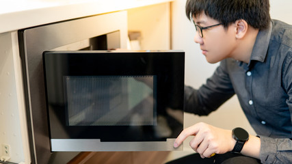 Fototapeta na wymiar Asian man opening microwave door in the kitchen showroom. Buying cooking appliance for domestic kitchen. Home improvement concept