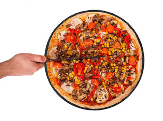 The chef cuts the pizza with a kitchen knife. Delicious pizza with mushrooms, corn, cherry tomatos, courgettes and bell peppers on the slate plate, isolated on white background, top view