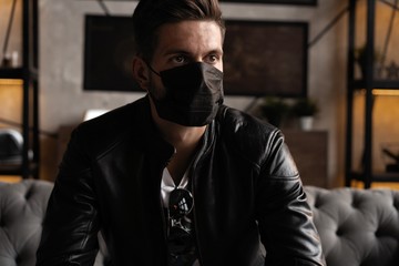 Handsome young manin black mask. Fashionable man in leather jacket standing and looking at window