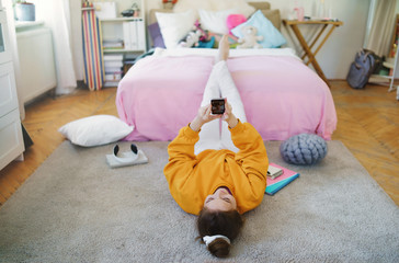 Young girl with smartphone on floor at home, making video call.