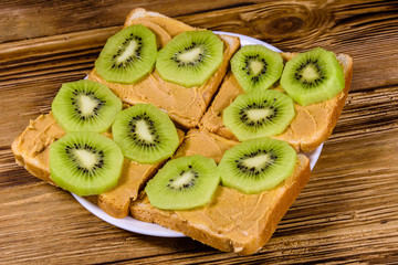 Sandwiches with peanut butter and sliced kiwi fruits in plate on a wooden table