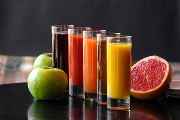 Orange, Apple, tomato, carrot, cherry juice in glass glasses on a black background with apples, grapefruit and mint