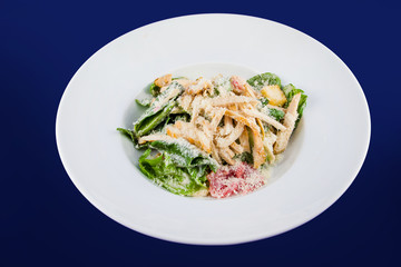 Plate with fresh caesar salad. Closeup on a white plate on a blue background.