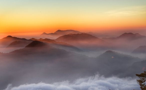Scenic View Of Silhouette Mountains During Foggy Weather Against Orange Sky