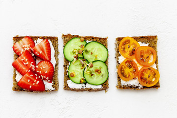 Three toast with strawberry, cucumber, tomatoes, cream cheese and fresh herbs, top view. Organic healthy food concept