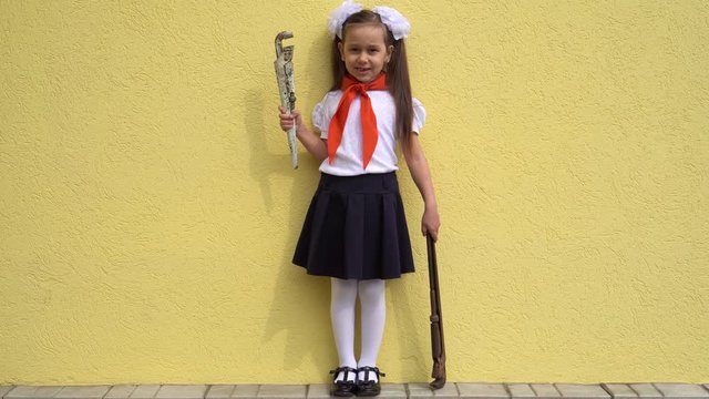 A little girl of 7 years old in a school uniform and a red tie on her neck holds construction tools in her hands on a yellow background. The concept of the history of Russia, pioneers and the celebrat