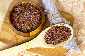 Top view of brown raw dry flax seeds in a wooden spoon and bowl on a light background.