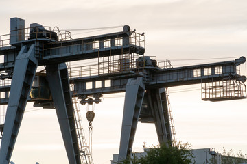 two large bridge cranes on the background of the sky at sunset. Outline of a girder crane on a...
