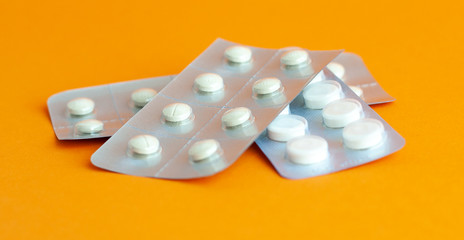 White tablets in a gray pack lie on an orange surface. Close up.