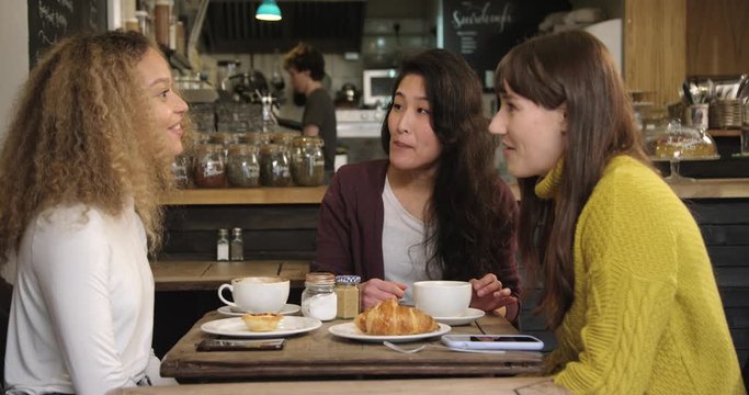 Group Of Female Friends Chatting And Laughing At Table In Cafe
