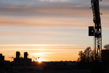 Evening outline of the city. The silhouette of the factory against the sky or sunset. The tower crane operates on the territory of the factory.