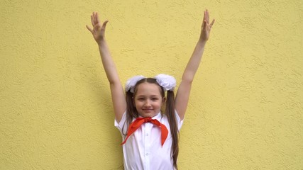 Girl schoolgirl teenager in a school uniform and a red tie on her neck stands with hands up on a yellow background. The concept of the history of Russia, pioneers and the celebration of labor day.