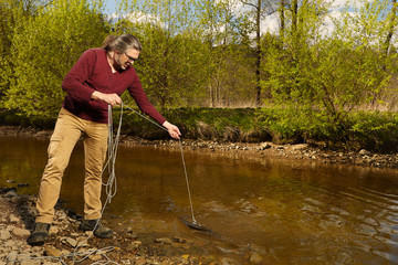 Man exploring river water by magnet on rope