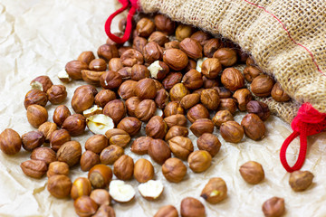 Peeled brown hazelnuts pour from the textile bag on light background.
