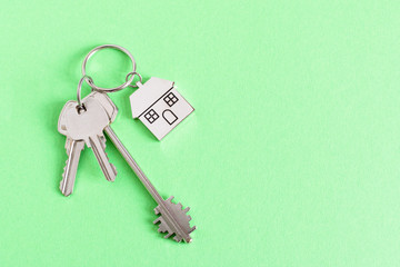 Key and keychain in a house shape on green background top view. Real estate concept.