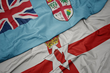 waving colorful flag of northern ireland and national flag of Fiji .