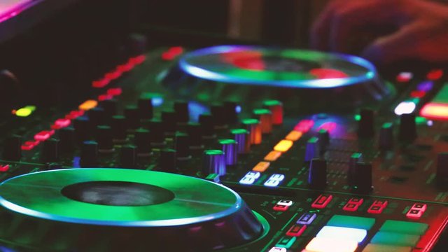 Close Up DJ hands playing music on sound console at dance party in nightclub. DJ mixer player and sound console for disco party. Disc jockey controller and mixing deck with colored illuminated 4k