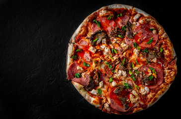 Pizza with Mozzarella cheese, salami, chicken meat, beef, ham, Tomato sauce, pepper, spices. Italian pizza on Dark grey black slate background
