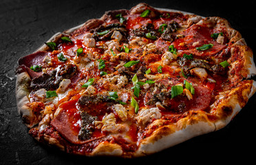 Pizza with Mozzarella cheese, salami, chicken meat, beef, ham, Tomato sauce, pepper, spices. Italian pizza on Dark grey black slate background