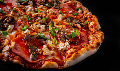 Pizza with Mozzarella cheese, salami, chicken meat, beef, ham, Tomato sauce, pepper, spices. Italian pizza on Dark grey black slate background