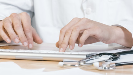 Fototapeta premium Hands of Doctor typing on keyboard of computer with stethoscope in a clinic, close up.