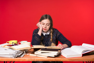 Schoolgirl is sitting at the table, on the table a lot of textbooks and notebooks, a girl was stole at hand, she was tired of studying