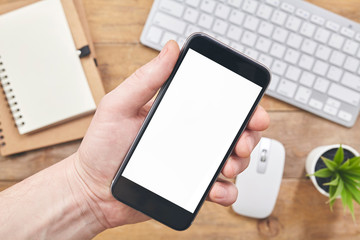 Man holding a phone with isolated screen over the desk in the office. Top view.