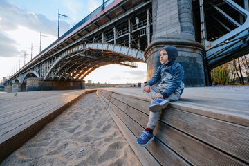 Portrait of a boy sitting on the beach near the bridge