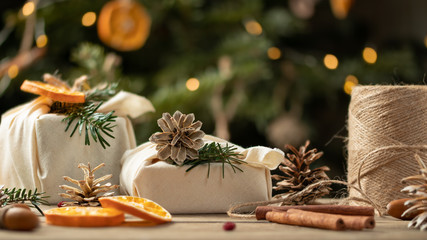 Zero waste christmas concept. Packed in natural fabric gifts and decorations from natural materials on wooden table near Christmas tree with lights