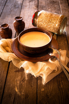 Boiled buckwheat with milk in wooden bowl on rustic wooden background, vertical image
