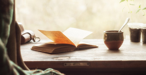 Cup of coffee and an open old book on a wooden windowsill