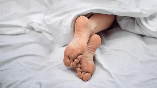 Close up bare female foot lying on comfortable bed under blanket. Shot on RED Raven 4k Cinema Camera