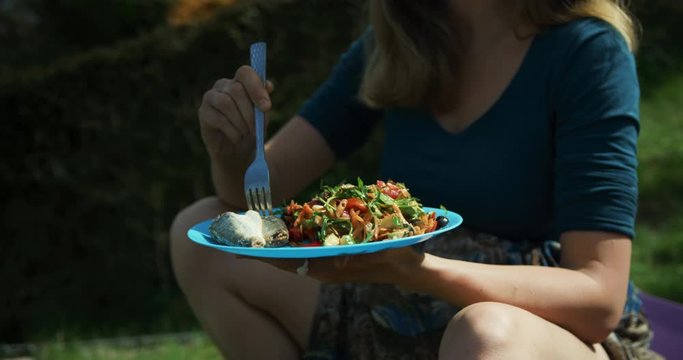 Young woman eating fish and salad for lunch in garden