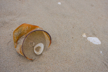 Fototapeta na wymiar Rusty plastic cup on a sand after sea storm. Garbage in the nature. Environmental pollution. Ecological problem