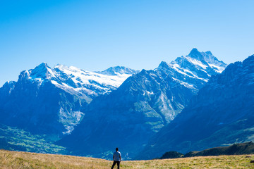 Man standing alone in a meadow facing the Swiss Alps
