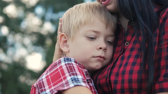 happy family mom and son sad child concept. mom tender childhood video. slow motion video. a lifestyle mom brunette girl protects caress gently hugs takes care of the son boy blonde outdoors