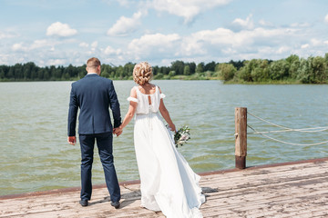 the bride and groom walk along a wooden pier on lake