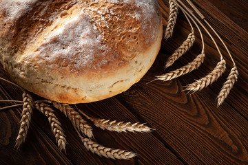 Homebaked bread. Loaf of round peasant bread and spikelets of wheat on a wooden background.