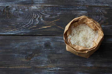 Raw white long-grain basmati rice in a craft bag on a wooden background, top view, space