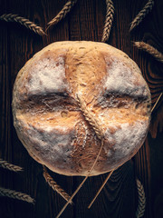 Homebaked bread. Top view of a loaf of round peasant bread and spikelets of wheat on a wooden background. Homemade baking.