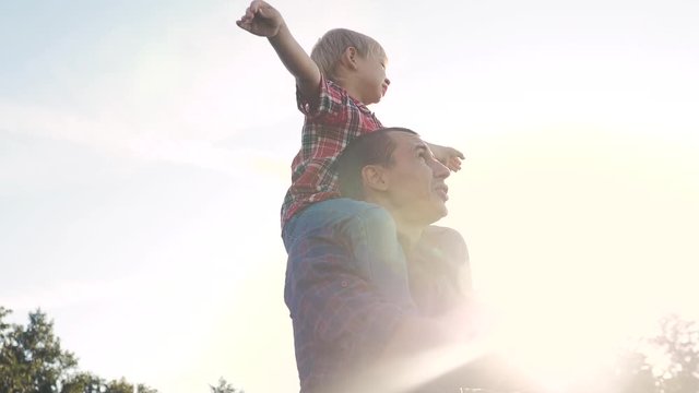 Happy Family Father Son Concept. Father Giving Son Ride On Back In Nature Outdoors . Portrait Of Happy Father Giving Son Lifestyle Ride On His Shoulders And Looking Up. Cute Boy With A Dad Playing