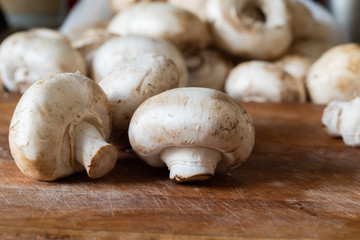 Fresh champignon mushrooms on the old wooden cutting board ready for frying. Side view. Close-up.