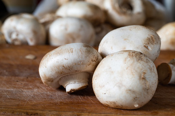 Fresh champignon mushrooms on the wooden cutting board ready for cooking. Side view. Close-up.