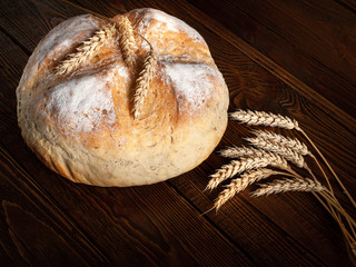 Homemade hot bread. Loaf of round peasant bread and spikelets of wheat on a wooden background.
