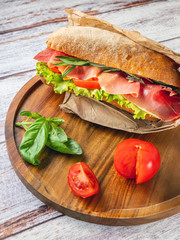 vertical view to ciabatta with prosciutto on wooden plate with basil leaves and tomatoes