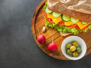 close up view to vegetarian ciabatta with radish and olives on wooden plate and dark background