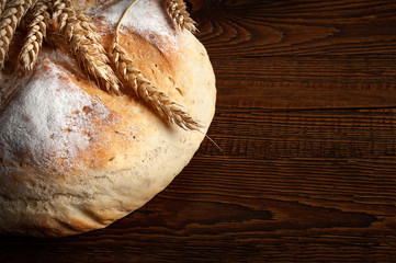 Close-up of homemade bread. Peasant round bread and wheat spikelets on a wooden background with space for text.