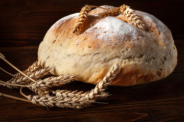 Homebaked bread. Closeup loaf of round fresh peasant bread and wheat spikelets on a wooden...