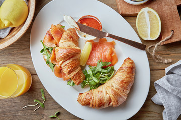 Fresh croissants sandwiches with salmon and arugula served with butter, lemon and orange juice on wooden tabletop. Delicious Breakfast. Top view