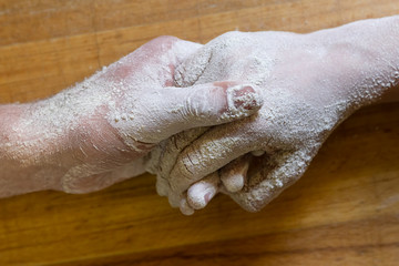 Male and female hands, covered in flour, holding each other against wooden table background
